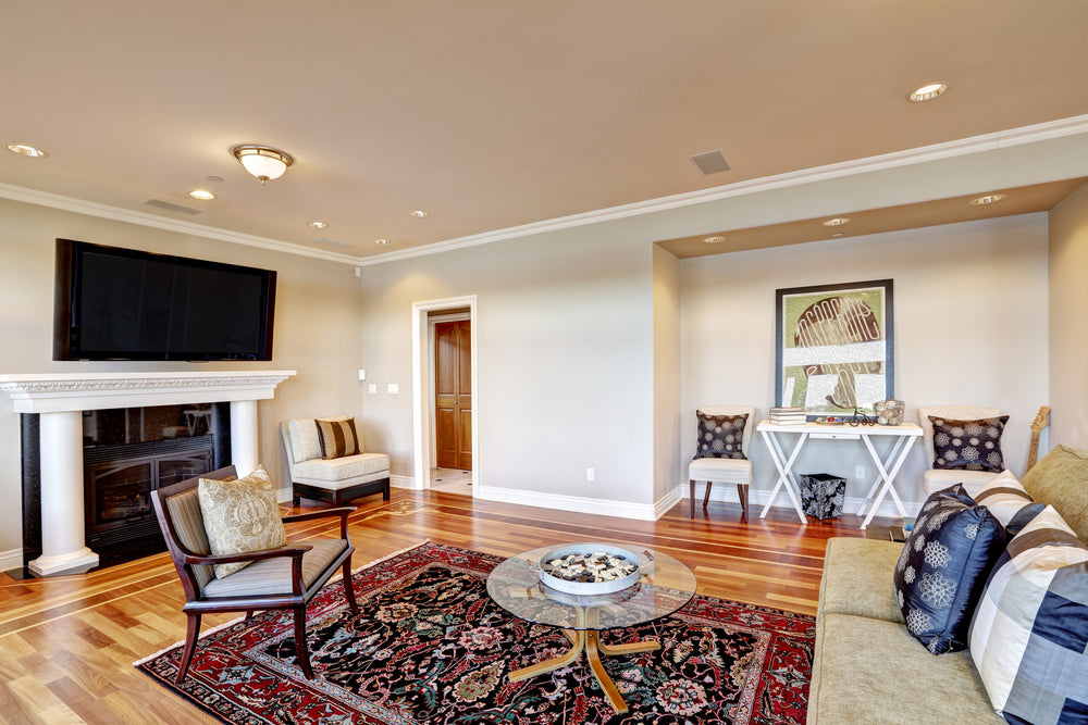 Lovely airbnb family room with cozy sitting area in wall niche, white column fireplace and accent bright colorful persian rug over polished hardwood floor.