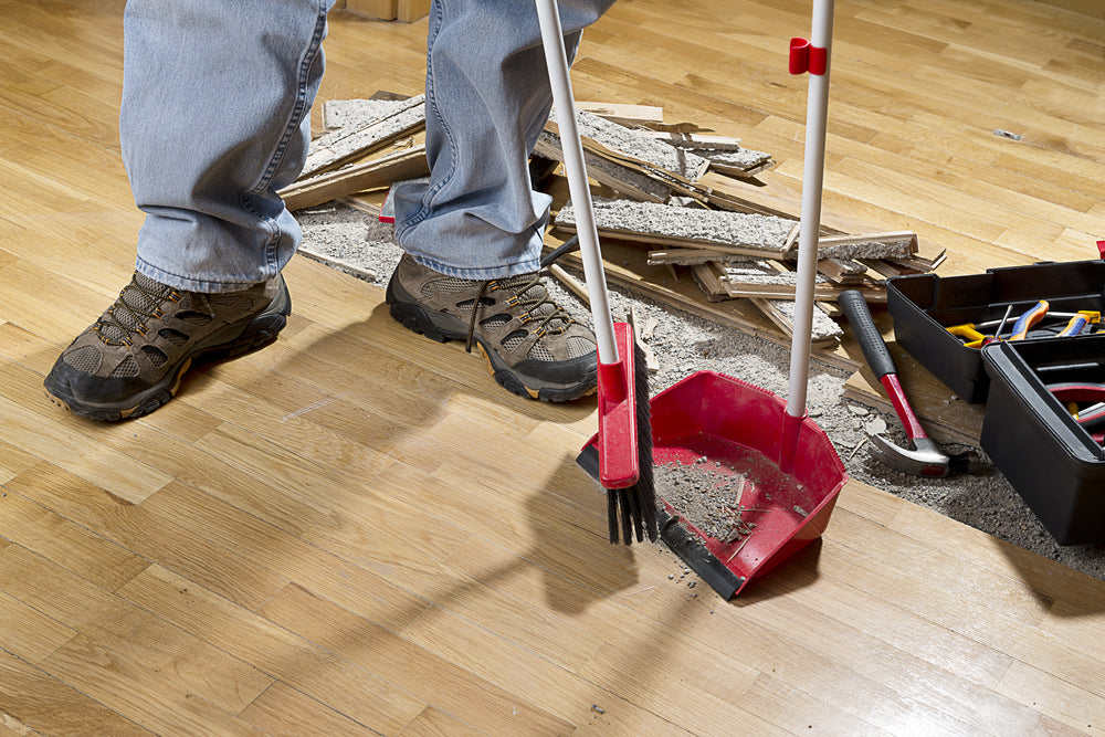 person with a broom sweeping floor into dustpan from hardwood