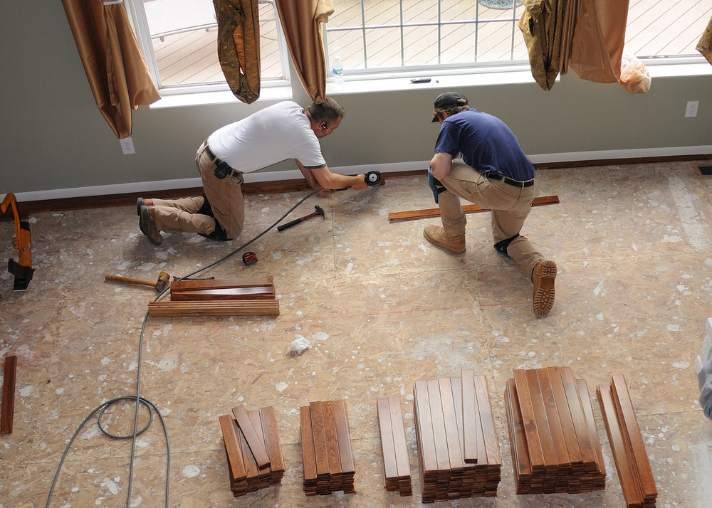 Construction workers install a hardwood floor over oriented strand board in a residence.