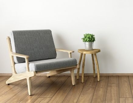 A room with hardwood floors and a matching chair and small table with a plant on it. The aesthetic of the room is very modern.